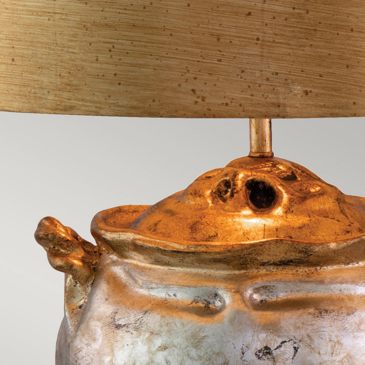 Here's an alternative version of the sentence using the provided product data:
Close-up of the Jackson 1 Light Table Lamp, showcasing a ceramic base with a rustic antiqued silver finish and gold leaf accents. The cylindrical lampshade above boasts a textured, speckled pattern that harmonizes with the earthy design, infusing this cast resin masterpiece with an artistic flair.