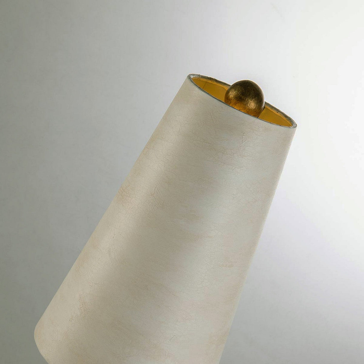 A Leda 1 Light Table Lamp in cream patina with a gold leaf interior is tilted against a plain background. Inside the top opening of the lampshade, a spherical gold element is visible, capturing the lamp's hidden charm.