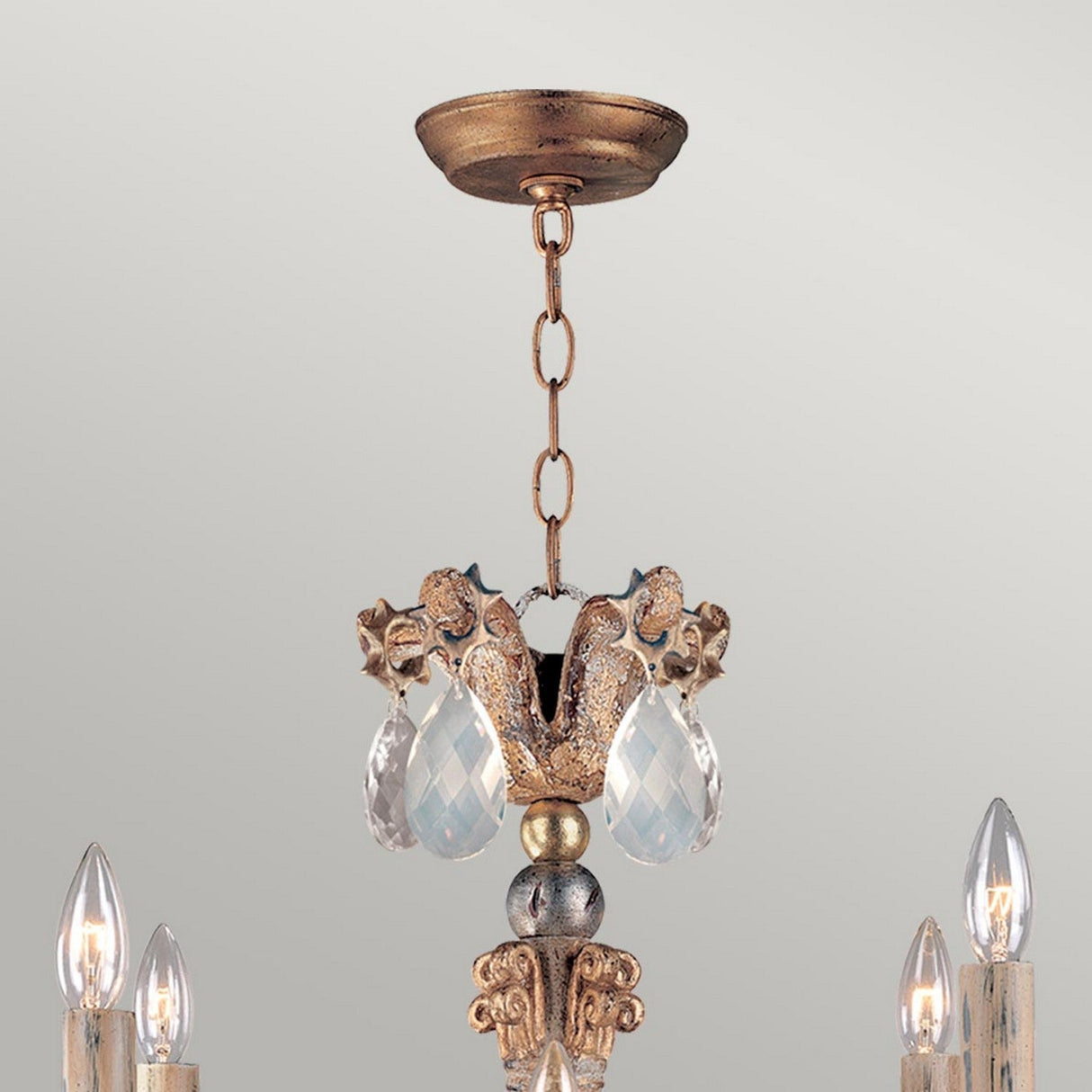 The Mignon 8 Light Chandelier - Gold & Silver showcases an exquisite gold and silver finish, adorned with radiant decorative crystal accents and sparkling crystal droplets. Candle-style light bulbs elegantly envelop the centerpiece, all gracefully suspended from an elegant chain connected to a stylish ceiling mount.