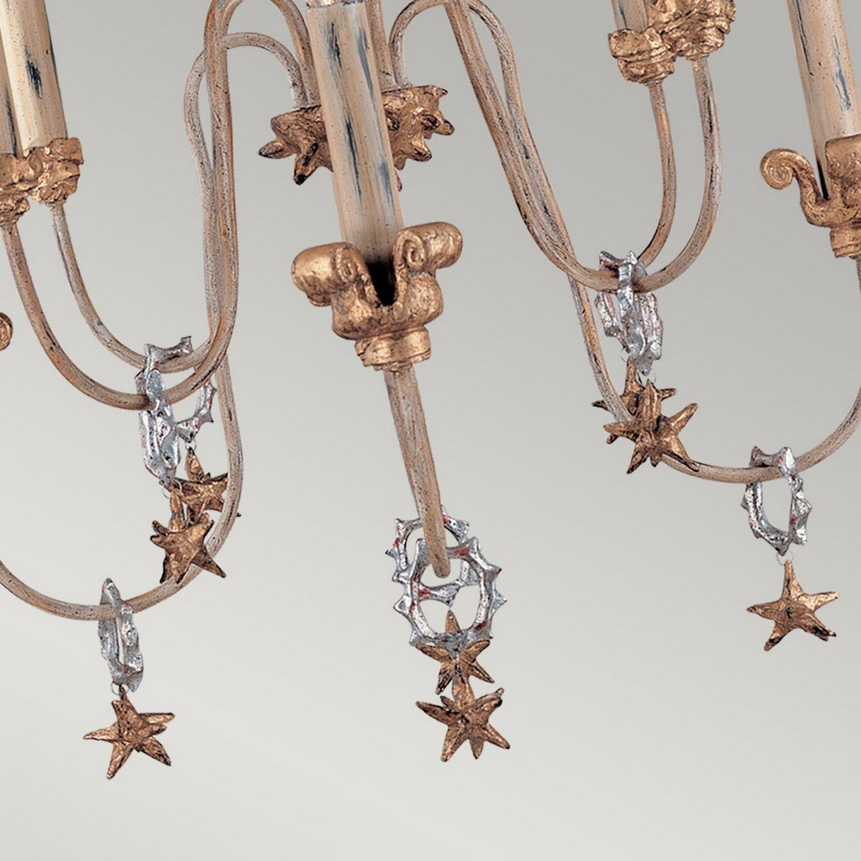 Close-up of the Mignon 8 Light Chandelier - Gold & Silver, featuring a gold leaf finish with silver star-shaped decorations, accented by crystal droplets hanging from its curved metal arms, set against a light gray background.