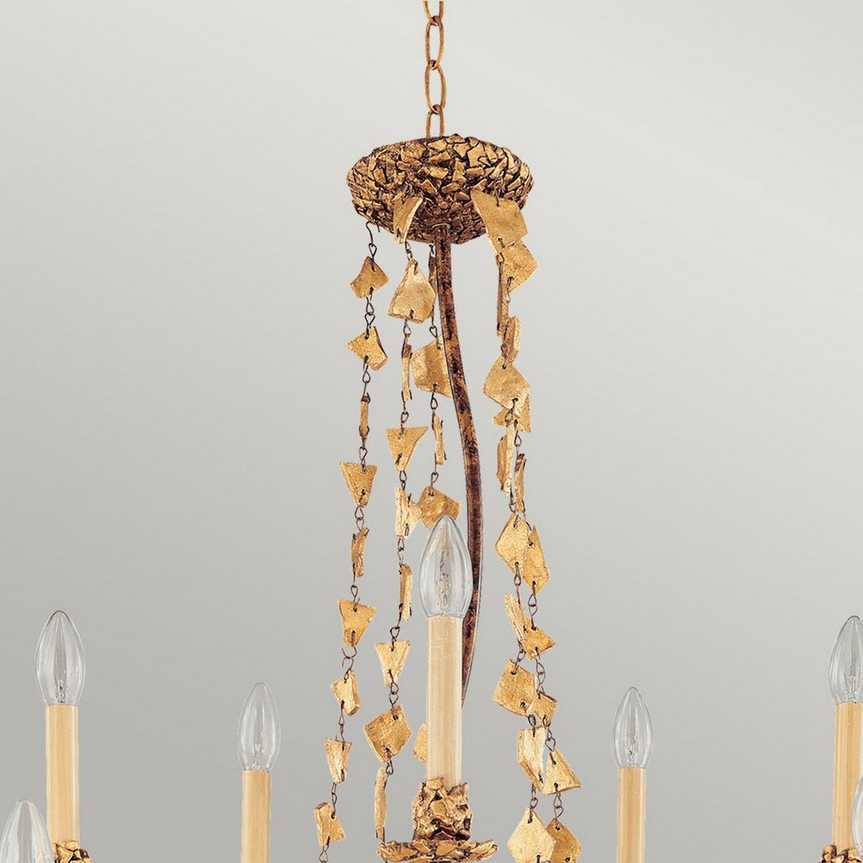 The Mosaic 10 Light Chandelier - Gold showcases a luxurious design with cascading chains adorned with leaf-like patterns. It features several candle-shaped lights extending from a circular base, providing an elegant look against a neutral backdrop.