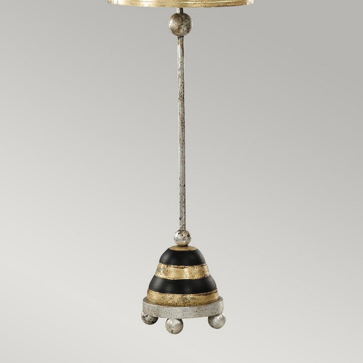 A metallic ornament resembling the Silver Leaf design, shaped like a bell with alternating black and silver stripes, is suspended by a thin rod. The bottom of the bell is accented with four small, rounded silver knobs. It shares similarities with the Phoenician 1 Light Table Lamp - Black, Gold & Silver Leaf. The backdrop features a plain, light gray color.