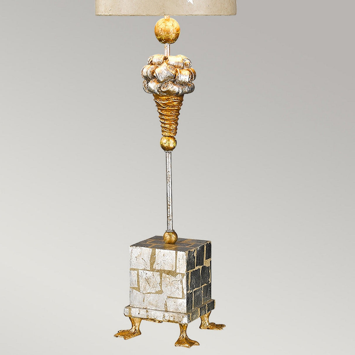 Introducing the Pompadour X 1 Light Table Lamp - Cream & Silver Leaf, an exquisite piece featuring a spiraled, gold and silver textured design reminiscent of an ice cream cone. It is elegantly topped with a finial that draws inspiration from a classic pompadour hairstyle and rests on a cube-shaped base adorned with brick-like patterns and supported by small, ornate legs.