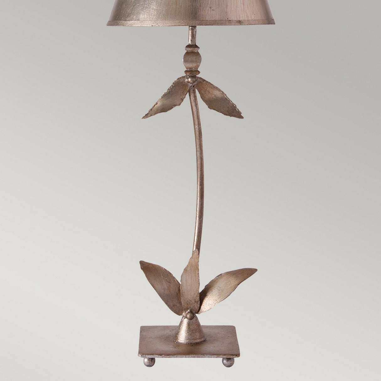 Introducing the Red Bell 1 Light Table Lamp in Silver Leaf finish with a stunning leaf-inspired design. This decorative metallic lamp features a slender stem adorned with two sets of angled leaf accents, complemented by a small, cone-shaped shade housing the light. Its vintage elegance is completed with a square base resting on small feet.