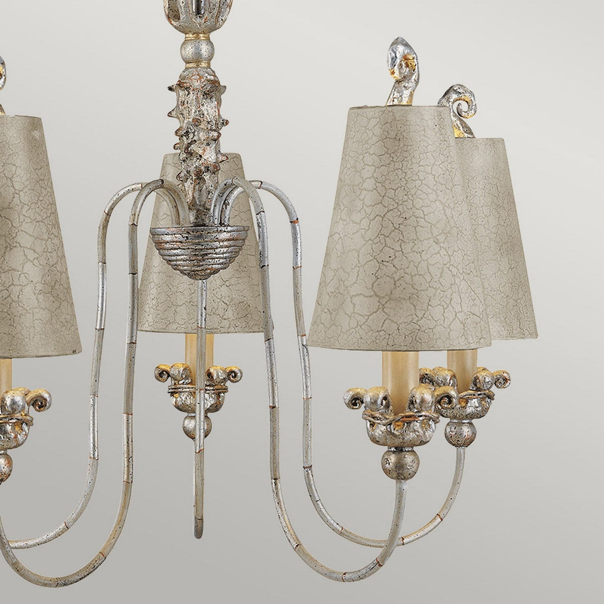 The Remi 5 Light Chandelier - Silver & Gold exhibits an elegant design with a detailed metallic framework and five arms, each supporting a bulb under a textured beige lampshade. Its traditional craftsmanship is highlighted by the intricate detailing and antique finish.