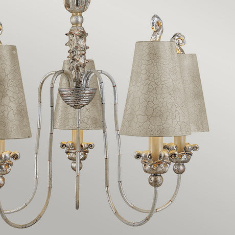 The Remi 5 Light Chandelier - Silver & Gold exhibits an elegant design with a detailed metallic framework and five arms, each supporting a bulb under a textured beige lampshade. Its traditional craftsmanship is highlighted by the intricate detailing and antique finish.