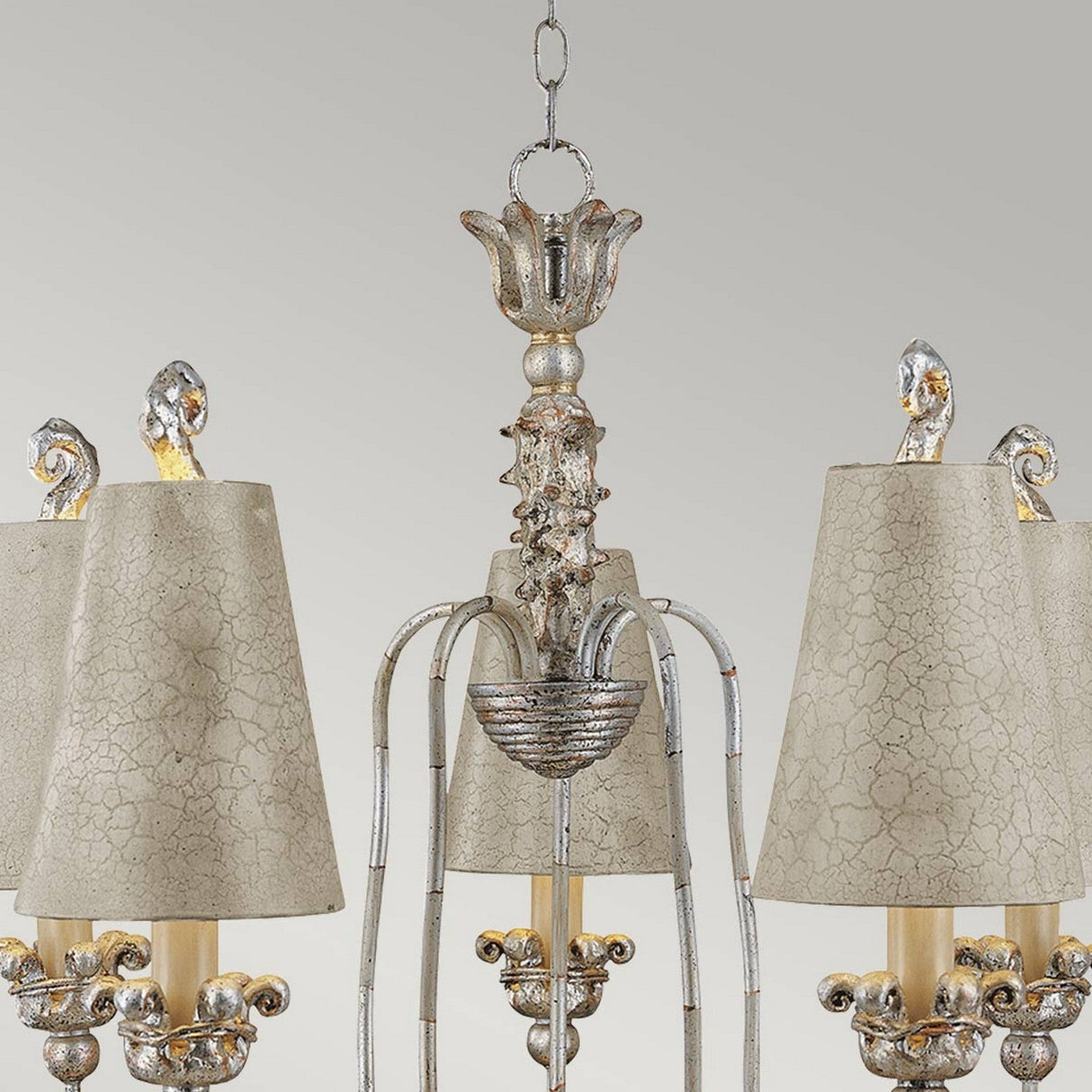 Explore the Remi 5 Light Chandelier in Silver & Gold, a stunning piece of traditional artistry featuring ornate metallic elements and five lampshades with a cracked texture. Its distressed, rustic finish combined with intricate scrollwork and floral motifs offers an elegant design ideal for any vintage setting.