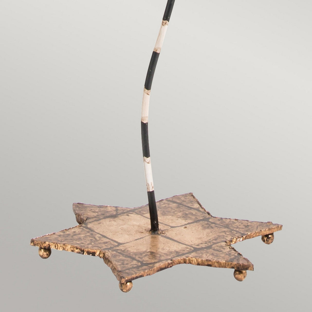A decorative star-shaped umbrella base emits tropical elegance with its weathered bronze finish and white stripe accents, echoing the refined allure of the South Beach 1 Light in Black, Putty, and Gold Leaf. Resting on small round feet, it stands out against a plain light gray background.