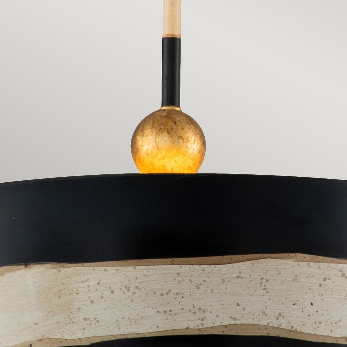 The South Beach 1 Light Pendant showcases a modern design with a round, golden bulb sitting atop a black and putty-colored lampshade adorned with textured, speckled patterns. It hangs from a slender rod, exuding coastal elegance and achieving a minimalist look against the gray backdrop.