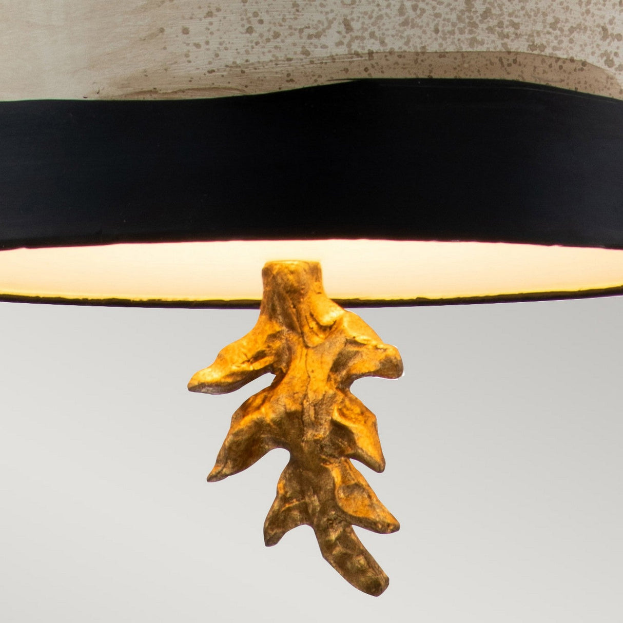 A close-up of the South Beach 1 Light Pendant, showcasing its curved, textured shade with a dark band at the bottom. A decorative element that resembles a small, golden root or branch hangs elegantly from the lamp, embodying coastal sophistication. The background features a light gray hue.