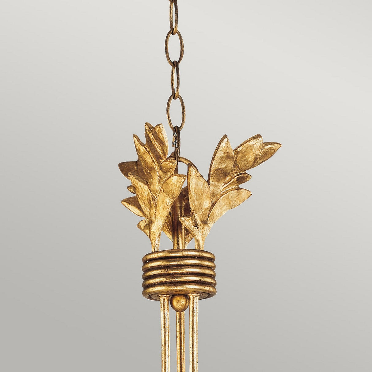 The Sweet Olive 3 Light Chandelier in Gilded Gold showcases leaf-shaped embellishments and a chain, with leaves sculpted in a metallic finish that accentuate its ornate and elegant design, while crystal medallions shimmer against a neutral backdrop.