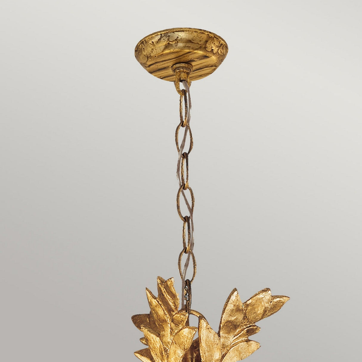 The Sweet Olive 3 Light Chandelier – Gilded Gold hangs elegantly, featuring a crystal medallion and leaf-shaped accents, against a light gray background.