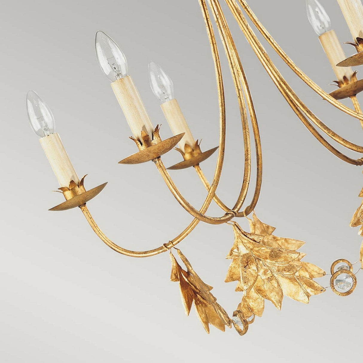 The Sweet Olive 6 Light Chandelier - Gilded Gold elegantly displays leaf designs and candle-shaped light bulbs against a neutral background. Its intricate detailing enhances the ornate appearance of the chandelier.