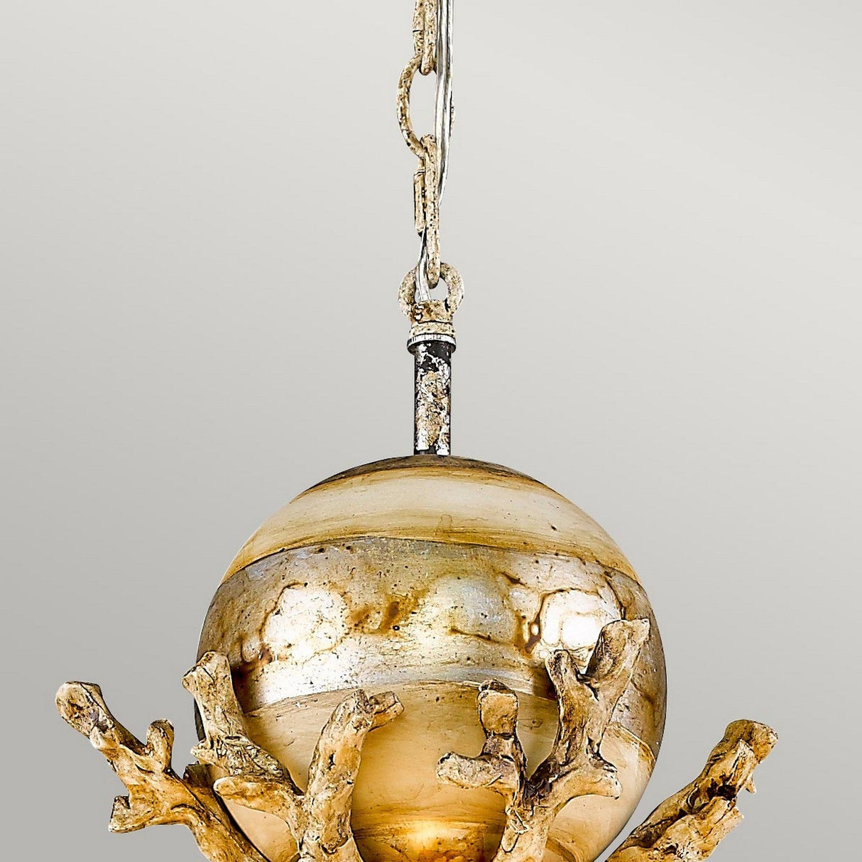 Introducing the Trellis 1 Light Pendant in Putty Patina & Silver Leaf, a decorative piece featuring a globe-shaped, gold-toned fixture adorned with abstract branch-like structures encircling the lower half. It is elegantly enhanced by a silver leaf orb element and suspended from a chain against a plain background.