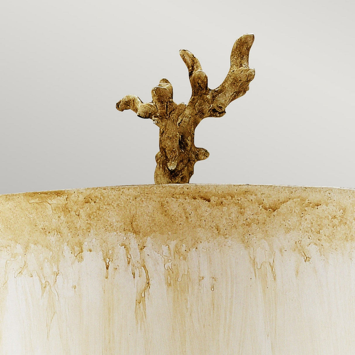 The Trellis 1 Light Table Lamp in Putty Patina & Silver Leaf, featuring a sculptural element reminiscent of a small, gnarled tree branch extending upwards, adorns a textured beige surface set against a neutral background.