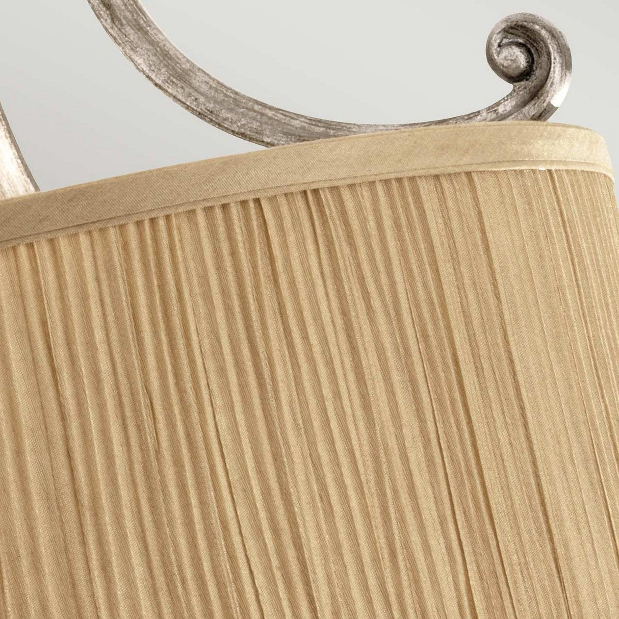 Close-up of a beige, pleated lampshade reminiscent of the Abbey 3 Light Semi Flush - Silver Sand design, featuring a metallic, spiral iron detail at the top against a light gray background.