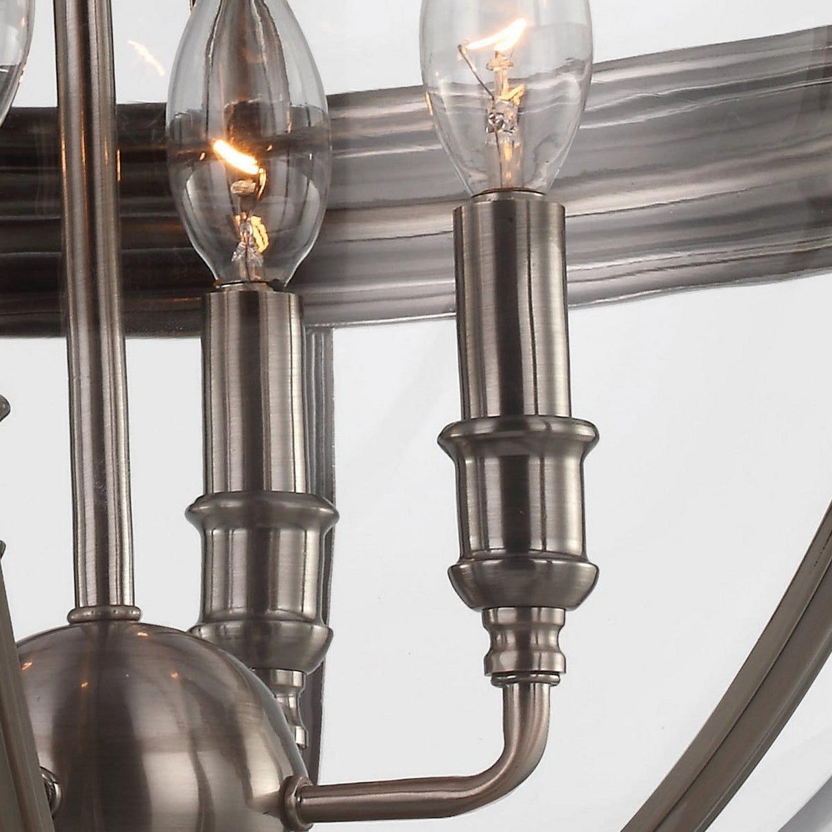 Close-up of the Adams 4 Light Chandelier - Antique Nickel, displaying four candle-shaped bulbs. The fixture boasts sleek, brushed metal arms and a reflective background, seamlessly blending Victorian-inspired elegance with a modern look.