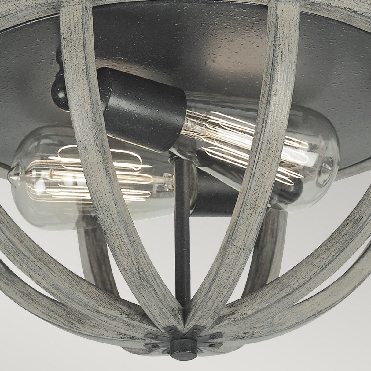 A detailed view of the Allier 2 Light Flush fixture highlights its rustic charm, combining weathered oak wood with an antique forged iron metal cage. Inside, two vintage filament Edison bulbs are showcased, enhancing its stylish design.