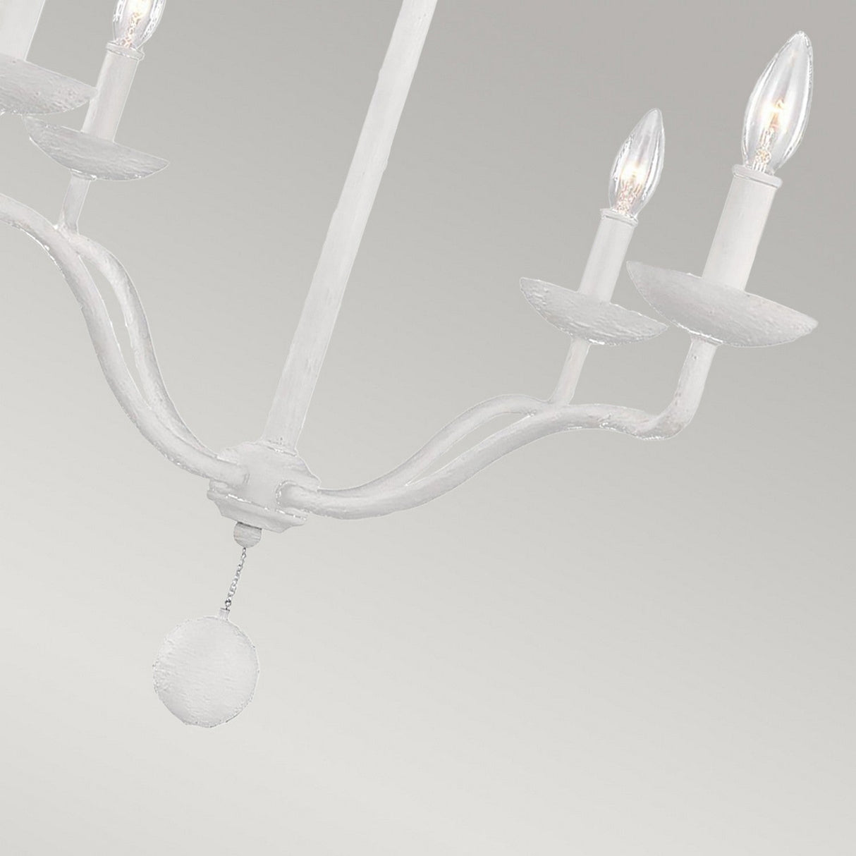 The Annie 4 Light Chandelier - Textured Plaster White showcases coastal-inspired elegance through its white design and three gracefully curved arms holding candle-shaped bulbs. Its charm is enhanced by a textured plaster finish and a central round decoration, all set against a light gray backdrop.