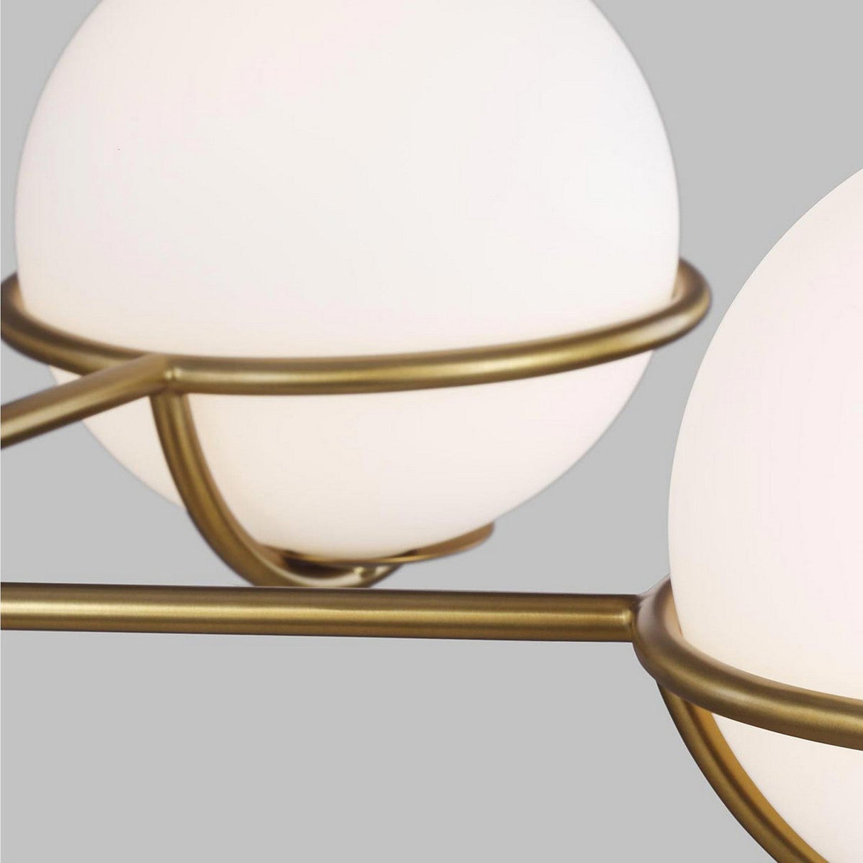 A close-up view reveals the modern charm of spherical light fixtures featuring frosted glass globes and burnished brass frames set against a gray background. The Apollo 5 Light Chandelier - Burnished Brass enhances this aesthetic with its white opal etched glass, offering a sleek and minimalist accent to the partially visible globes.