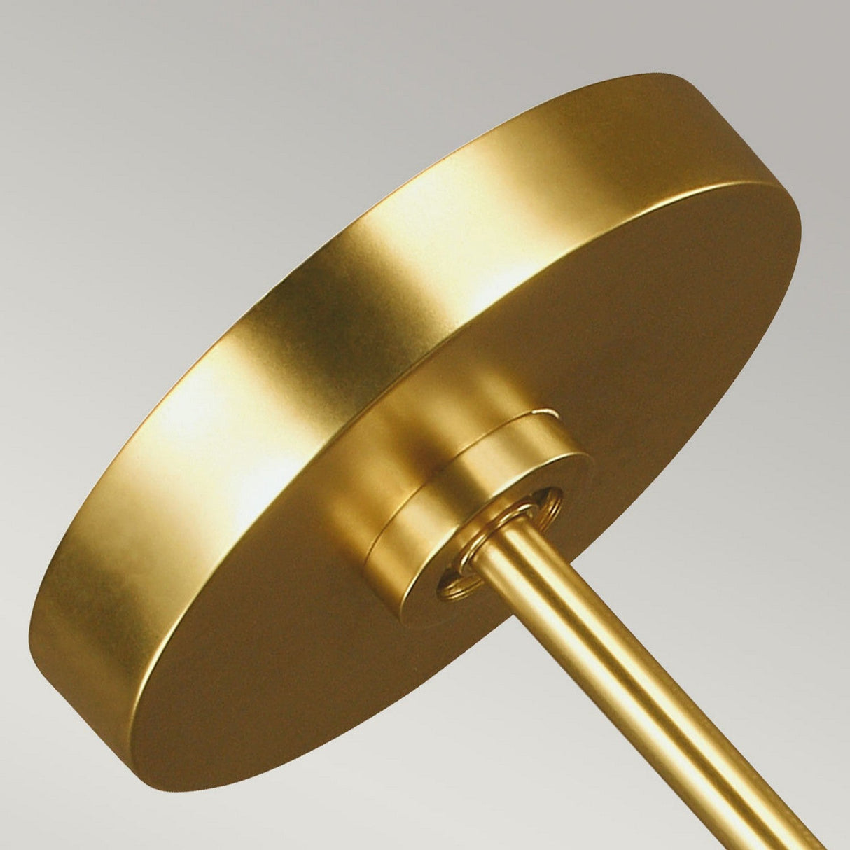 Close-up of a modern circular pendant light fixture featuring a burnished brass finish and sleek design, reminiscent of the Apollo 5 Light Chandelier - Burnished Brass, set against a neutral gray background.