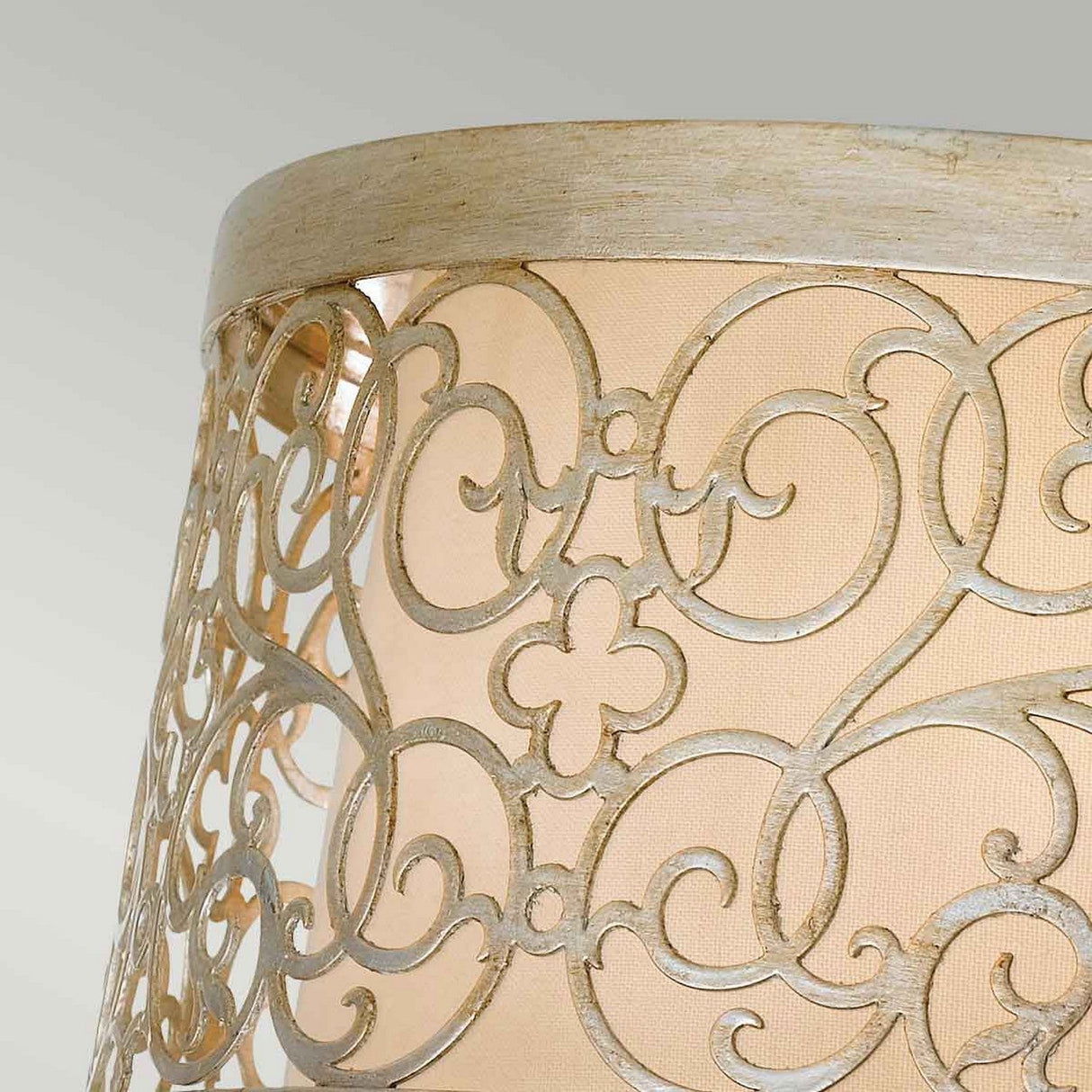 A detailed view of the Arabesque 2 Light Flush shows its elaborate lampshade, showcasing laser-cut scrollwork with floral patterns. Placed against a light beige background, the Silver Leaf Patina finish enhances its vintage elegance.