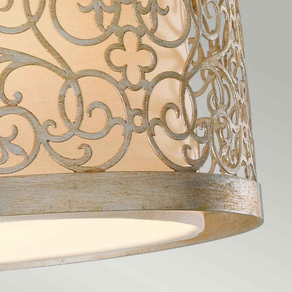 Close-up of the Arabesque 2 Light Flush, showcasing its elegant lampshade adorned with intricate, vintage-style laser-cut scrollwork. The metal frame, coated in Silver Leaf Patina, surrounds light-colored fabric that emits a warm glow. The background features a soft, neutral gradient.