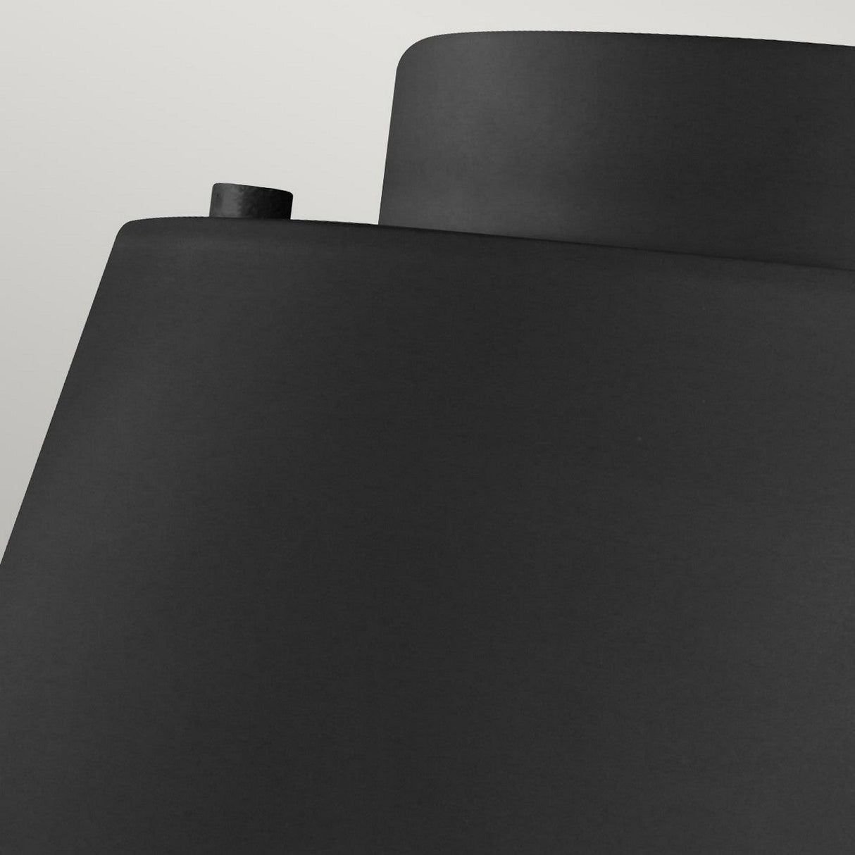 A close-up of the Asher 3 Light Flush in Midnight Black & Gold highlights its minimalist design with smooth, curved surfaces and a small cylindrical protrusion on the top left. The artwork is beautifully illuminated by ambient lighting against a soft, light gray background, enhancing the contrast with its deep midnight black hue.