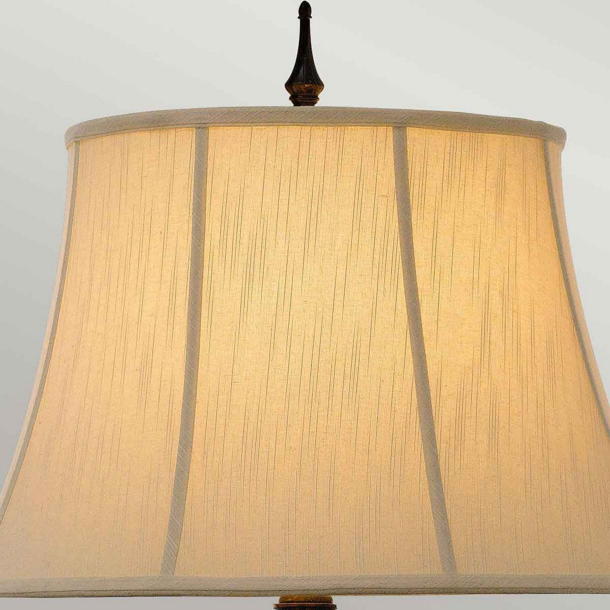 The Augustine 1 Light Table Lamp in Antique Brown boasts a beige fabric lampshade adorned with vertical stitching detail and a decorative finial, embodying a classic design. It provides a warm, soft glow that is perfect for transitional interiors.