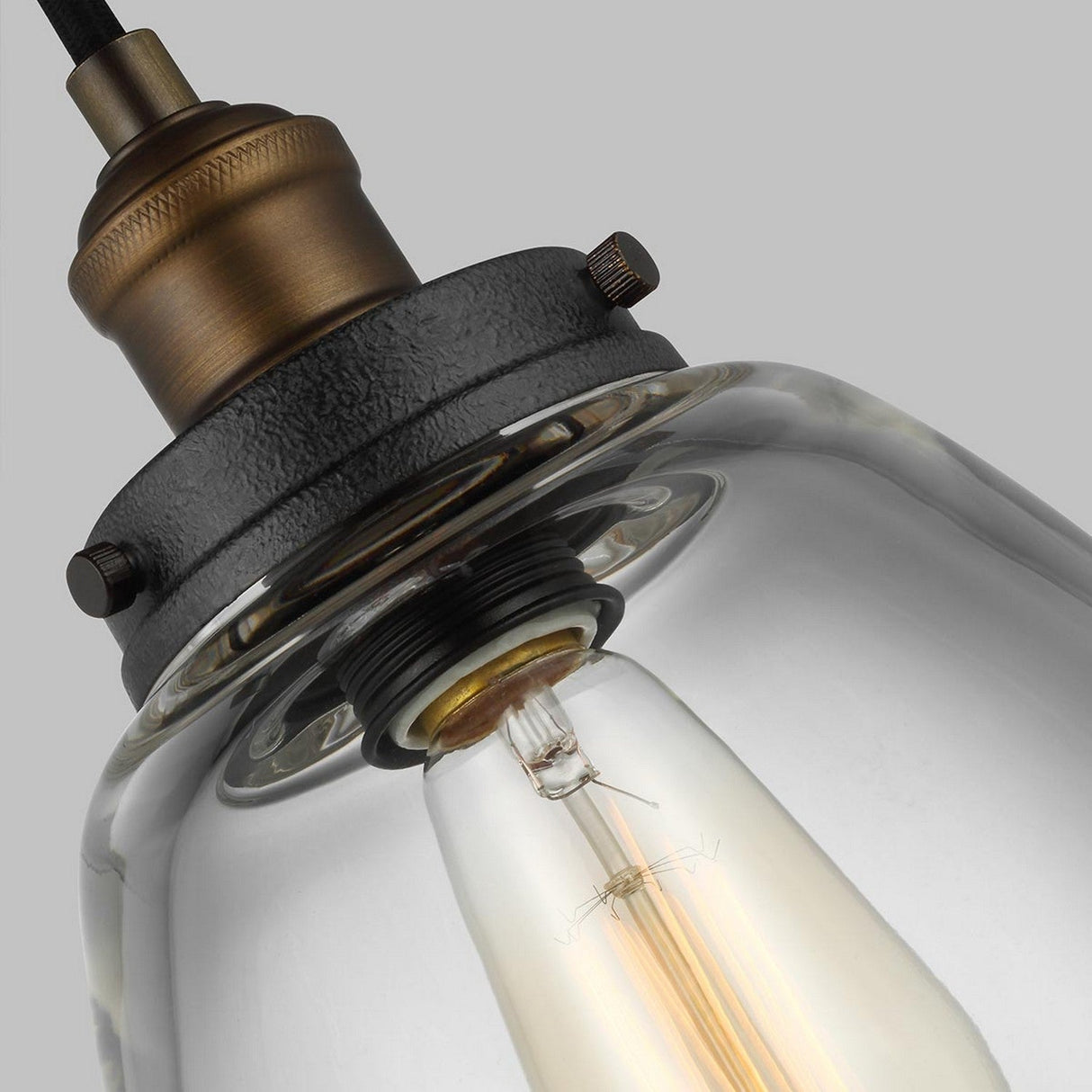 Capture the essence of the Baskin-2 1 Light Pendant, showcasing its vintage charm with a clear glass shade and exposed filament bulb set against a gray backdrop. The fixture harmoniously combines dark weathered zinc with painted aged brass accents to deliver a timeless elegance.