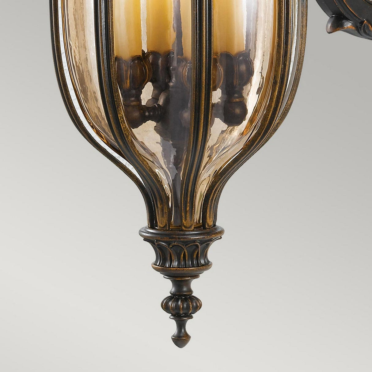 A close-up of the Baton Rouge 4 Light Outdoor Large Wall Lantern in a walnut finish, showcasing its intricate antique-style design with a glass bulb cover and ribbed detailing. Its warm amber tint enhances the vintage appeal, while the light gray background beautifully highlights this large wall lantern.