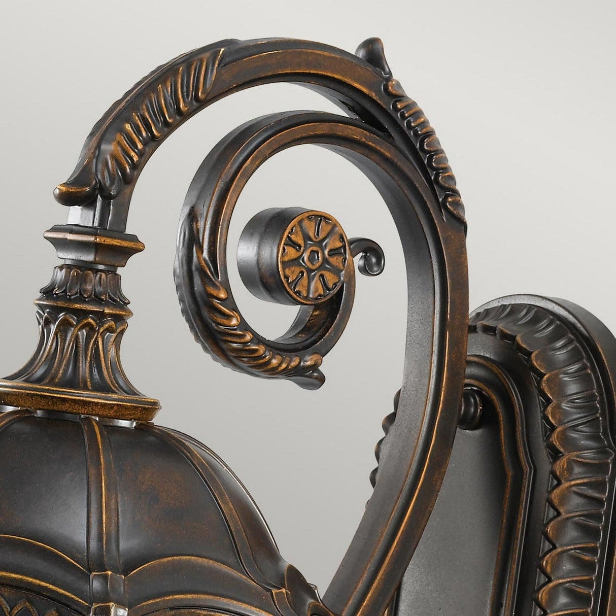 A close-up image showcases the Baton Rouge 3 Light Outdoor Medium Wall Lantern, featuring an ornate, antique-style design in black metal with intricate scrollwork and detailing. It boasts a rustic walnut finish and is set against a plain, light gray background, reflecting the charming elegance of Baton Rouge craftsmanship.