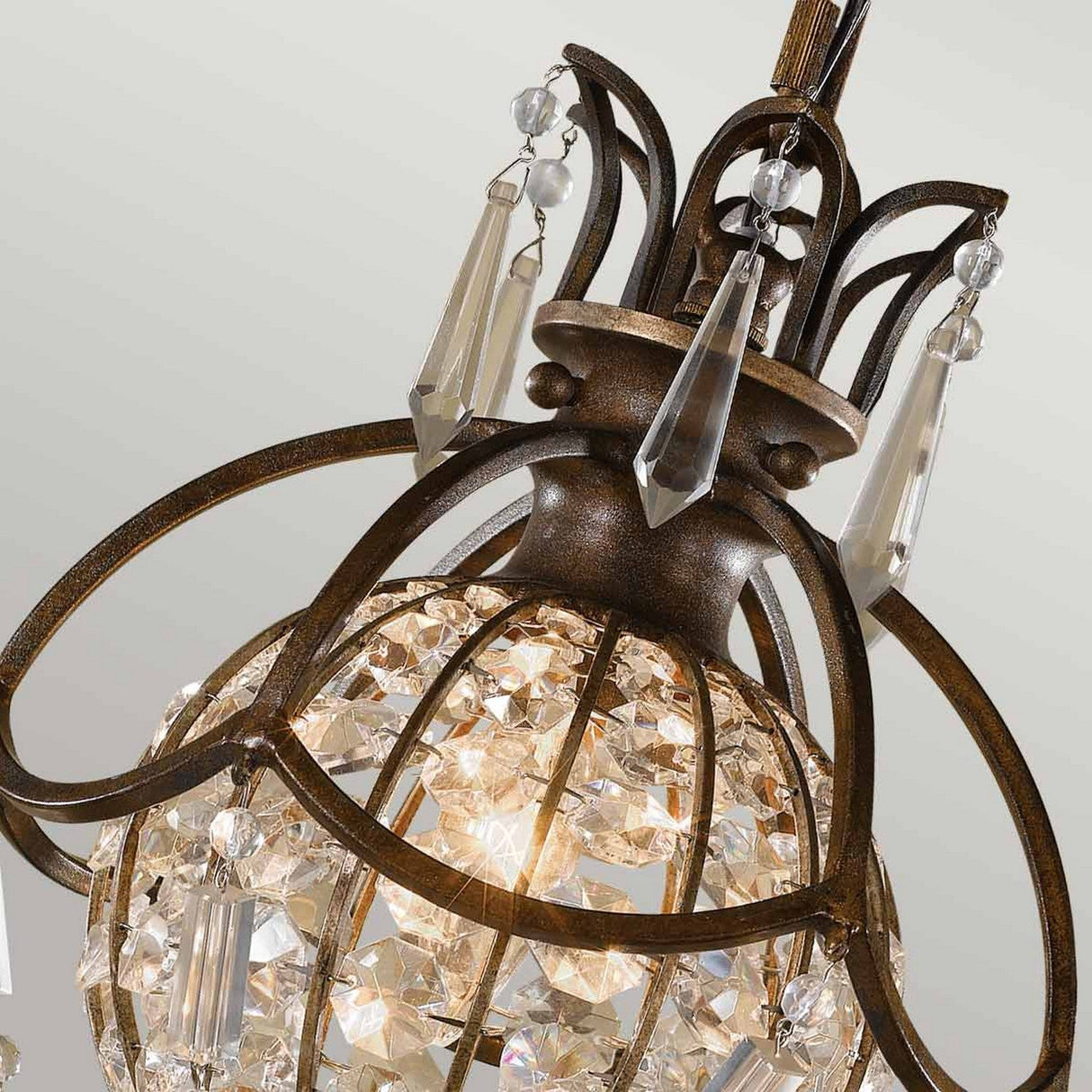 Close-up of the Bellini 1 Light Pendant Light in oxidized bronze/British bronze, showcasing an ornate metal cage design adorned with hanging antique quartz crystals and an illuminated globe with sparkling crystals inside, set against a neutral background.