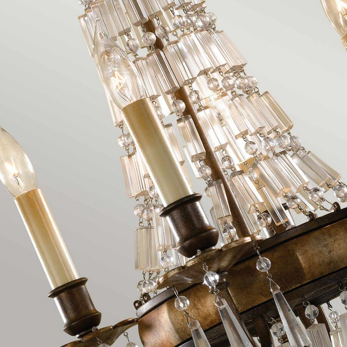 Close-up of the Bellini 4 Light Chandelier - Oxidized Bronze/British Bronze, showcasing its intricate details. The fixture includes several candle-like bulbs and multiple antique quartz crystal prisms arranged in tiers, creating a sophisticated and elegant appearance. An oxidized bronze finish complements the neutral background perfectly.