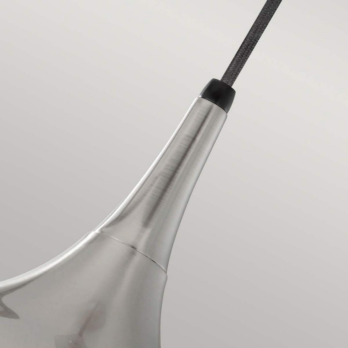 Close-up of a modern Beso 1 Light Medium Pendant - Brushed Steel suspended from a cord against a plain gray background. The brushed steel fixture features a sleek finish with a smooth, curved design, seamlessly blending contemporary style with retro lighting elegance.