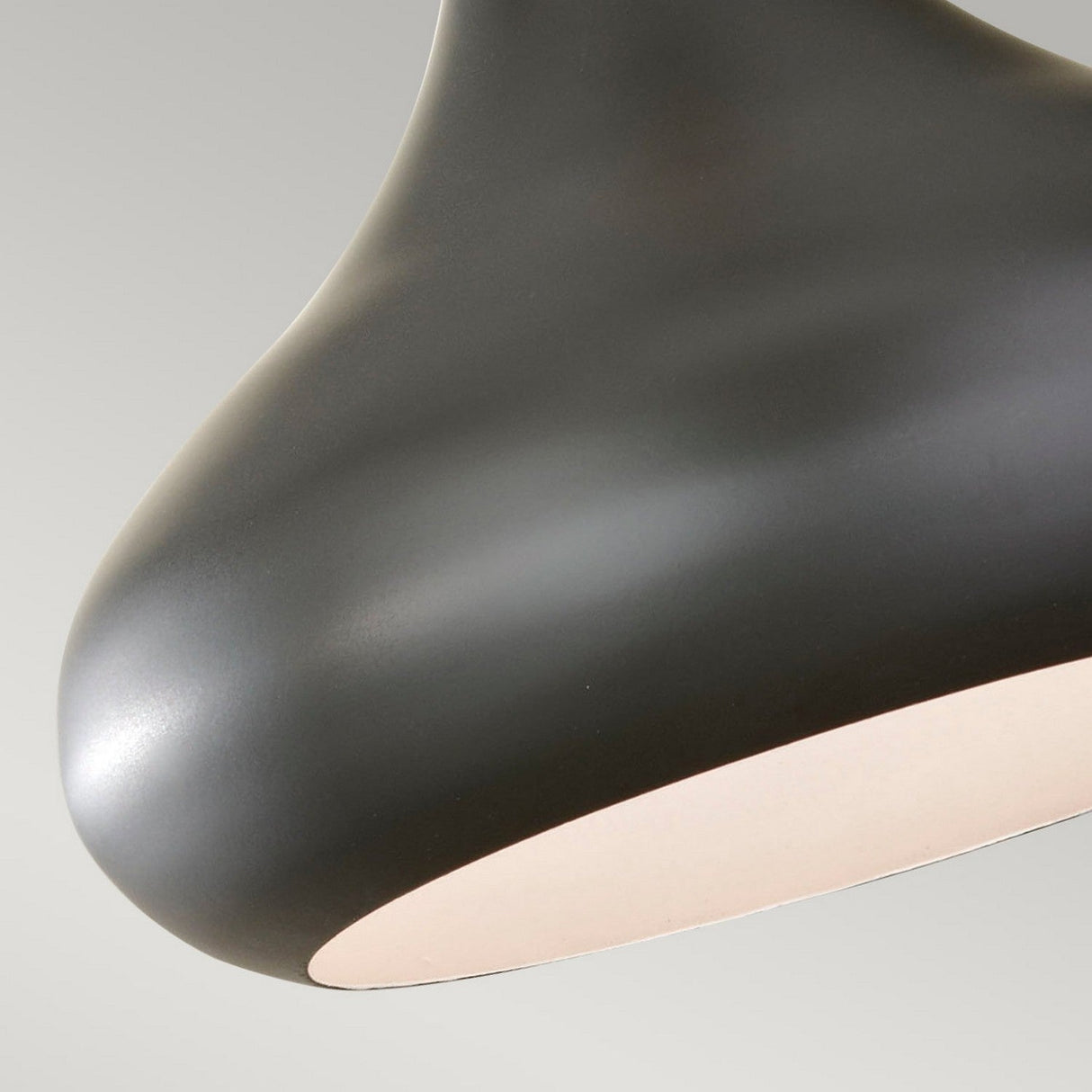 Close-up of the sophisticated Beso 1 Light Medium Pendant in dark bronze against a softly lit gray backdrop. The fixture boasts a smooth, curved design with a white interior that gently reflects light, making it ideal for infusing modern and minimalist style into contemporary spaces.