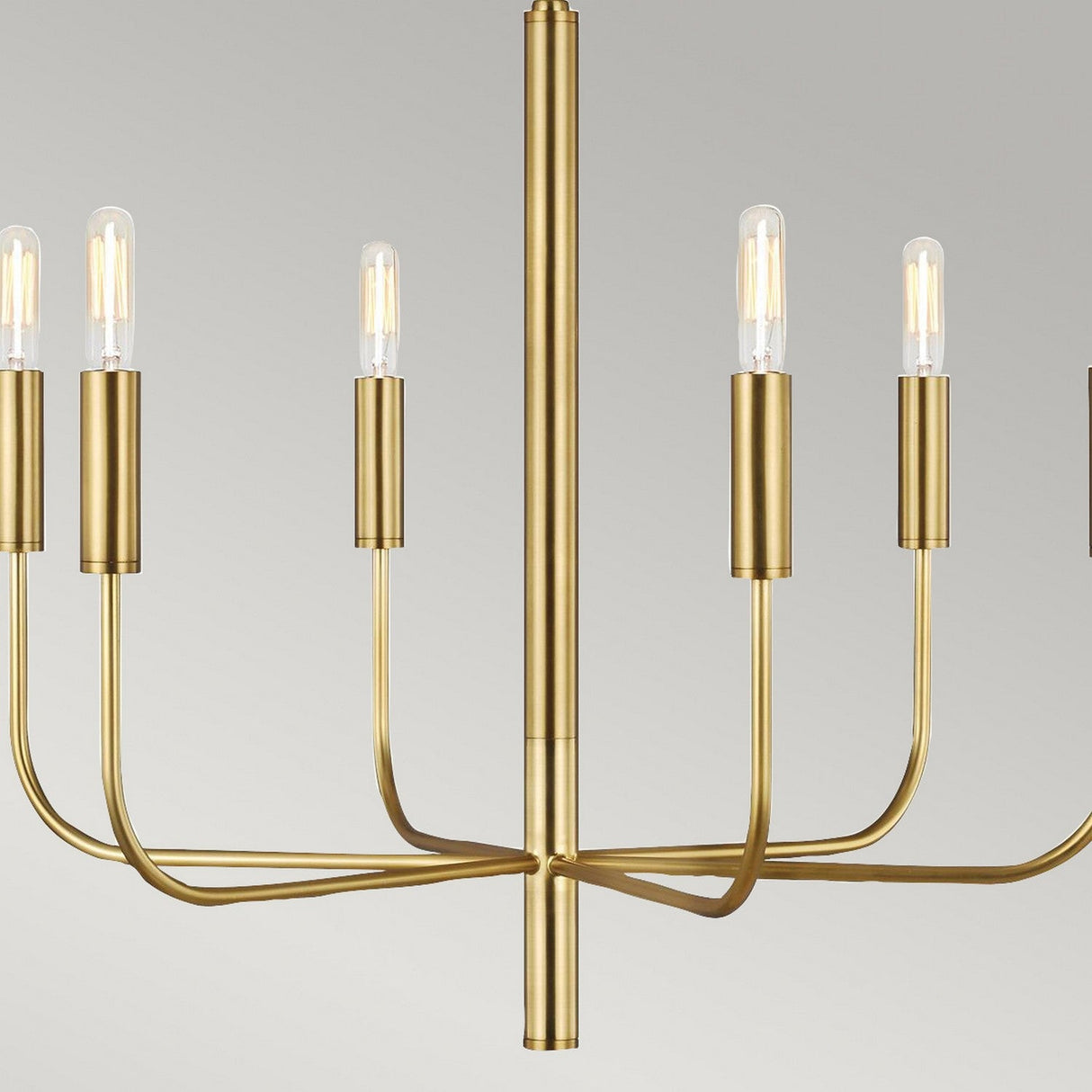 The Brianna 6 Light Chandelier - Burnished Brass exemplifies modern elegance with its sleek finish and minimalist design. Its multiple curved arms gracefully support exposed light bulbs, crafting a sophisticated appearance against a neutral backdrop.