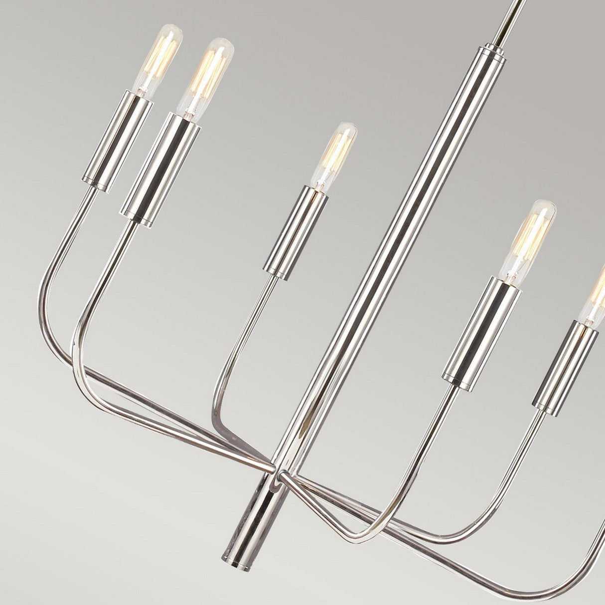 The Brianna 6 Light Chandelier - Polished Nickel is a modern lighting masterpiece, featuring six exposed bulbs elegantly positioned on sleek, curved arms. Its polished nickel finish and light gray gradient backdrop enhance its minimalist allure and contemporary charm.