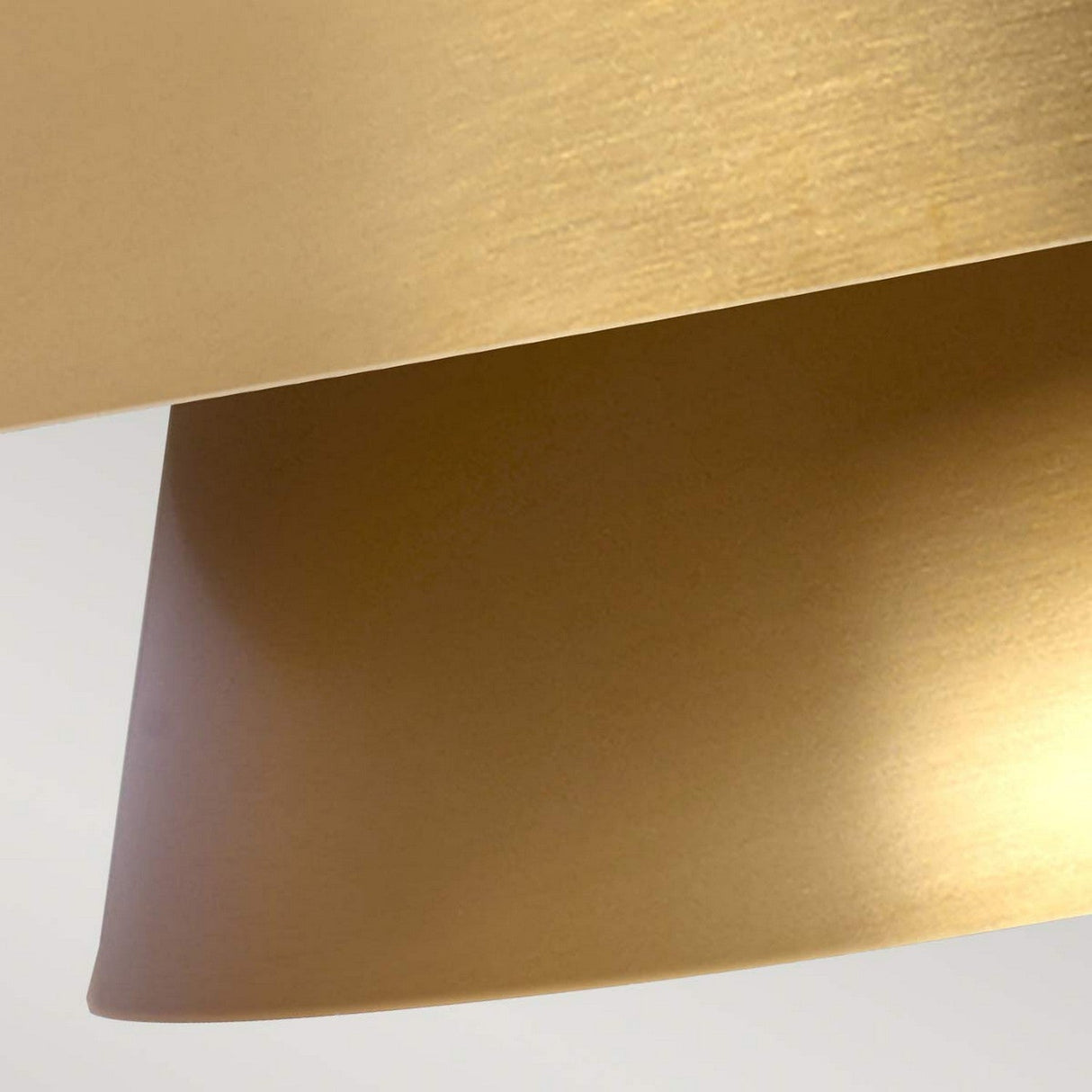 A close-up of two overlapping surfaces showcases the Brisbin 1 Light Pendant in Burnished Brass, with its brushed gold finish evoking a Mid-Century Design. The modern and sleek appearance is enhanced by ambient lighting that highlights the texture and curves, casting subtle shadows.