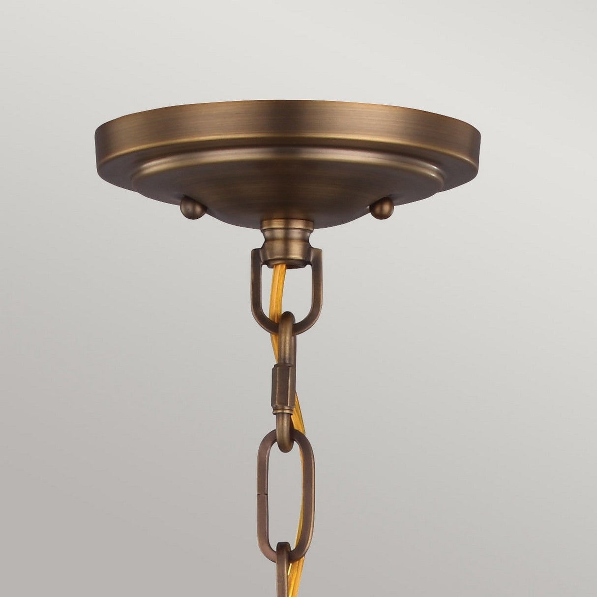 Close-up of the Cadence 1 Light Mini Pendant in Dark Antique Brass and Matte Black, exuding a vintage-industrial vibe. It features a metal chain with an electrical cord hanging vertically from a circular base. The background is a plain, light-colored wall.