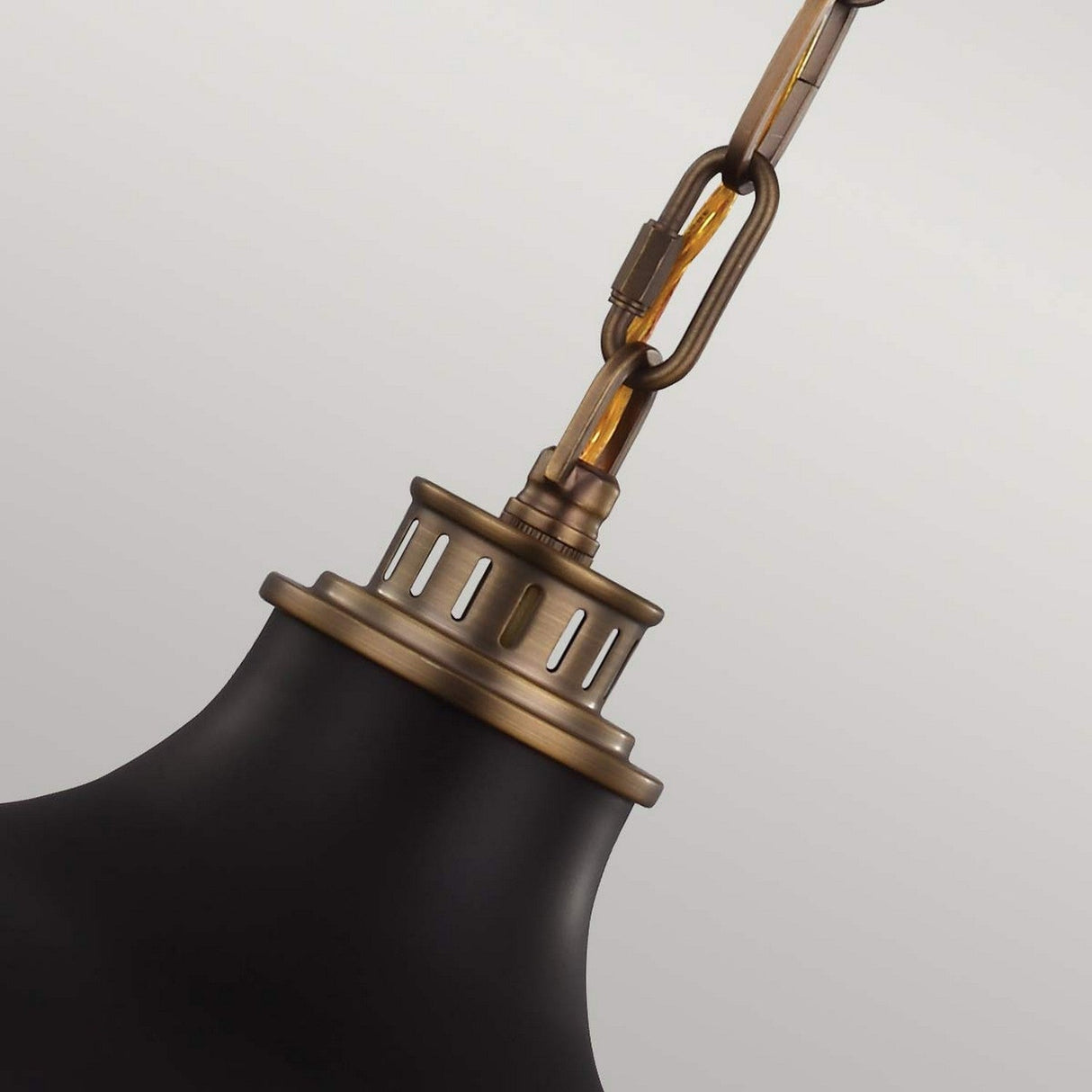 Close-up of the Cadence 2 Light Pendant, featuring a chain-linked design in dark antique brass and a matte black shade. This industrial lighting piece showcases a metallic finish, with its vintage style set against a neutral gray background.