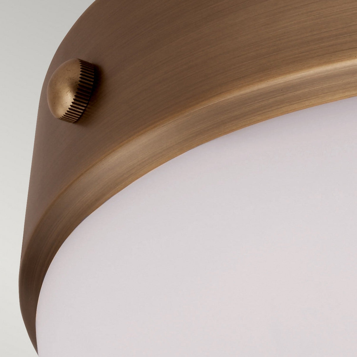 Close-up of the Cadence 2 Light Flush - Dark Antique Brass fixture, showcasing its antique brass finish. It features a frosted glass shade and a round side knob, capturing an industrial design with its sleek, curved surface.