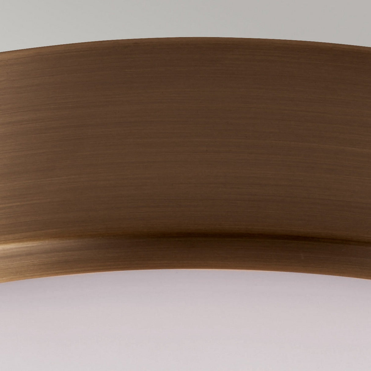 A detailed view of the Cadence 2 Light Flush in Dark Antique Brass showcases its smooth and subtly arched metallic surface against a gradient light background, exuding an industrial design charm.