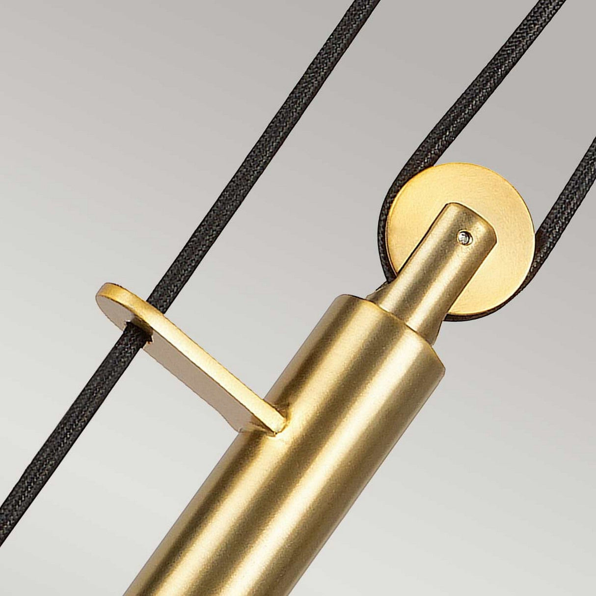 Close-up of the Candor 1 Light Pendant in matte white and brass, highlighting its modern cylindrical design with an adjustable feature. It boasts a metal rod and circular attachment point, with black cables providing a subtle contrast against the soft gray backdrop.