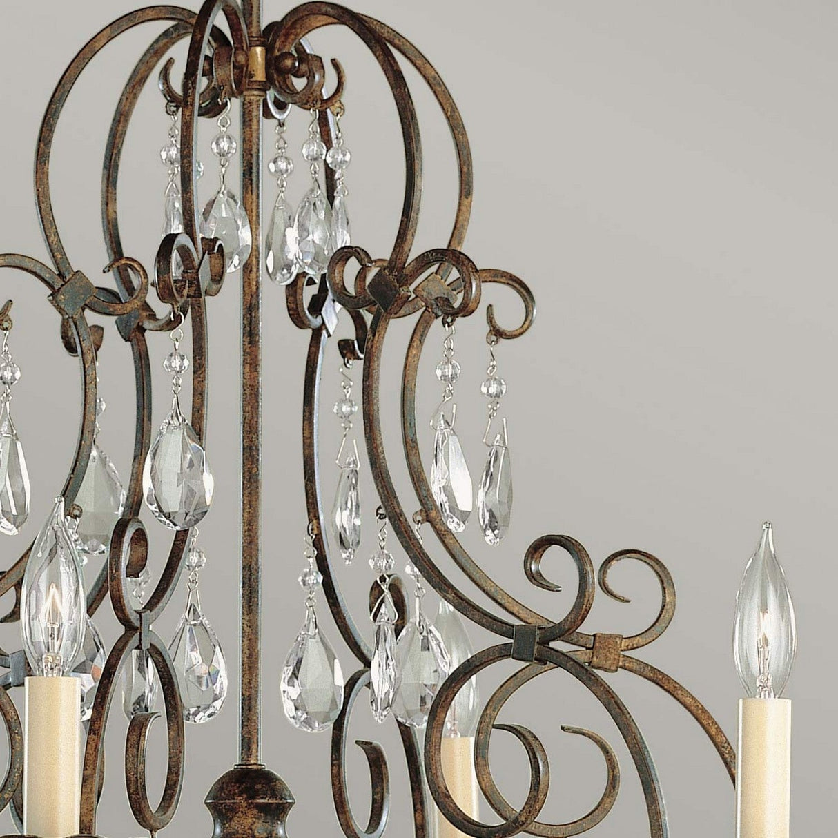 A close-up of the Chateau 6 Light Chandelier - Mocha Bronze features detailed metalwork in Mocha Bronze and hanging crystal accents. The chandelier is equipped with candle-shaped bulbs, offering an elegant contrast against a neutral backdrop.