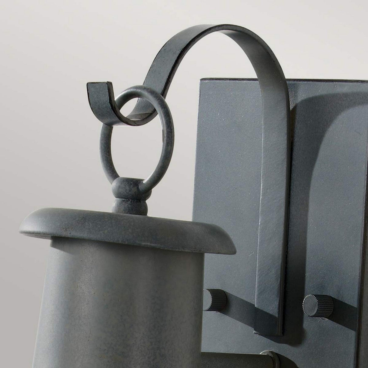 Close-up of the Chelsea Harbor 1 Light Outdoor Wall Lantern - Storm Cloud, featuring a vintage aesthetic with a curved hook design at the top, connected to a rectangular wall mount. This lantern offers a smooth finish and simple, elegant appearance, making it an ideal outdoor wall light against neutral gray surroundings.