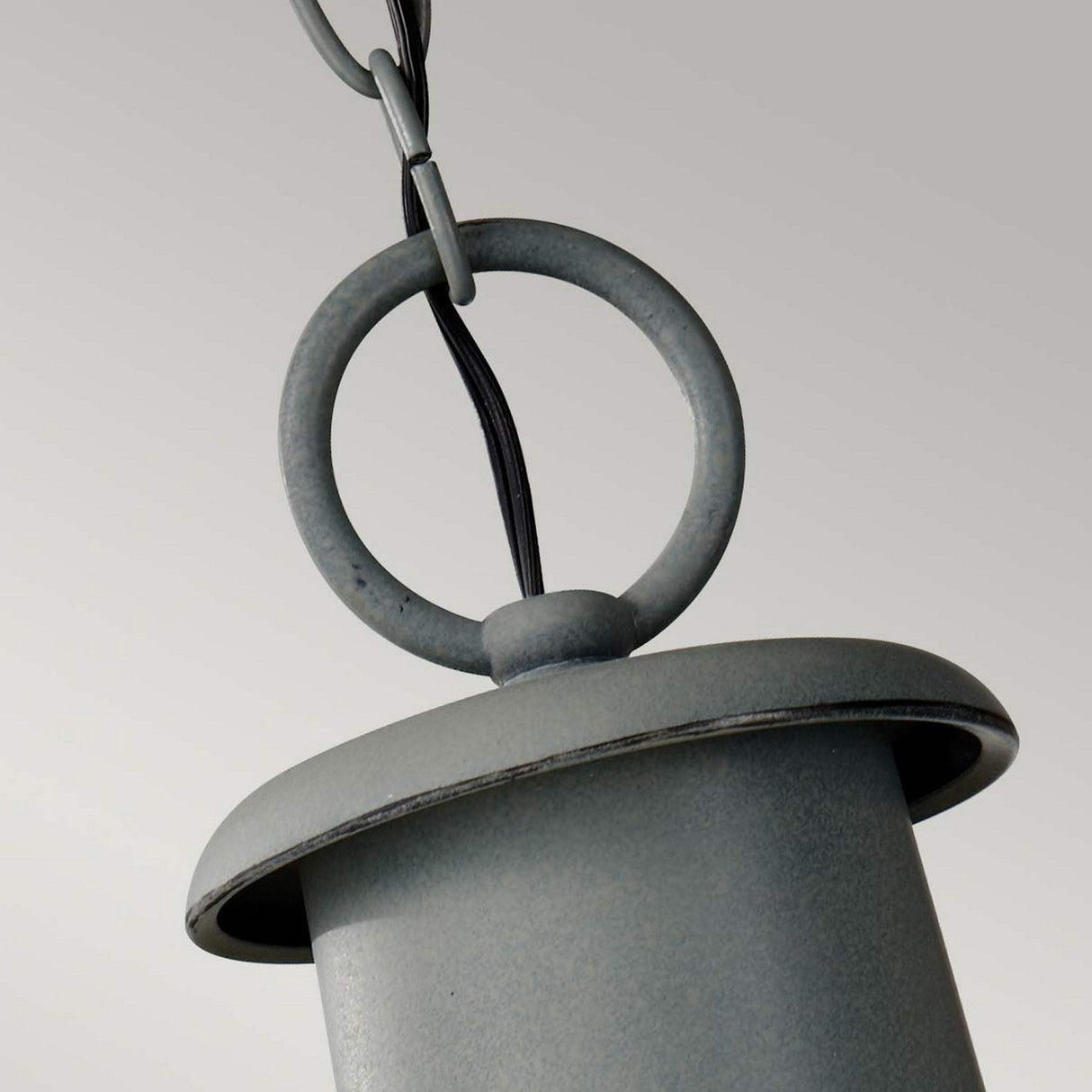 A close-up of the Chelsea Harbor 1 Light Outdoor Chain Pendant - Storm Cloud highlights its sleek, cylindrical design and gray metal finish. Featuring a circular ring at the top connected to a chain, this fixture radiates coastal industrial charm against a neutral backdrop.