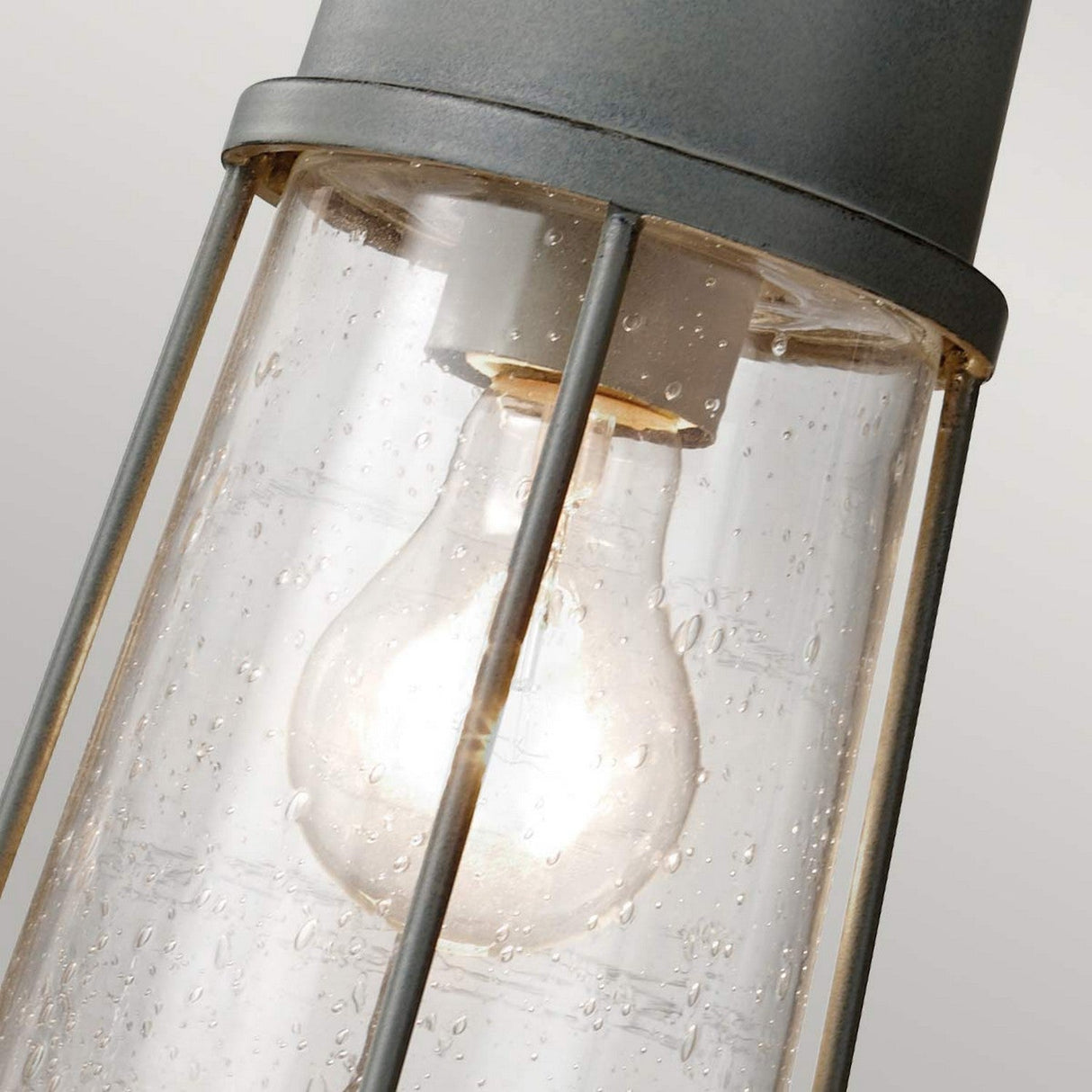 Close-up of the Chelsea Harbor 1 Light Outdoor Chain Pendant in Storm Cloud, showcasing a clear glass casing adorned with small water droplets. Inside, a glowing bulb exudes coastal industrial charm, encased by decorative metal bars for support.