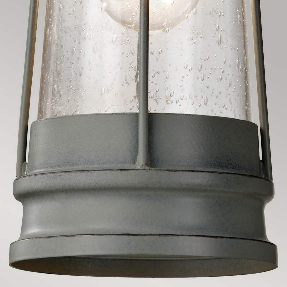 A close-up of a weathered outdoor lantern with raindrop-patterned glass and a gray metal frame exudes coastal industrial charm. The image captures the base, highlighting its rustic design similar to the Chelsea Harbor 1 Light Outdoor Chain Pendant - Storm Cloud, showcasing textured surfaces reminiscent of an outdoor chain pendant.