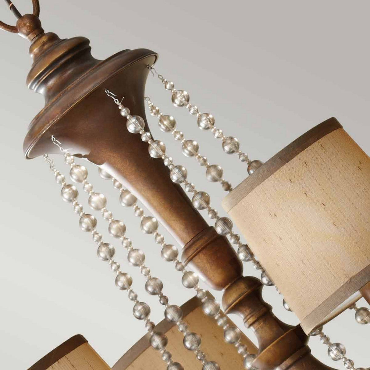 A close-up view of the Feiss Clarissa 6 Light Chandelier in a stunning Firenze Gold finish, adorned with strands of champagne-plated glass beads. This elegant fixture features multiple beige fabric lampshades, accentuating its classic design against a light background.